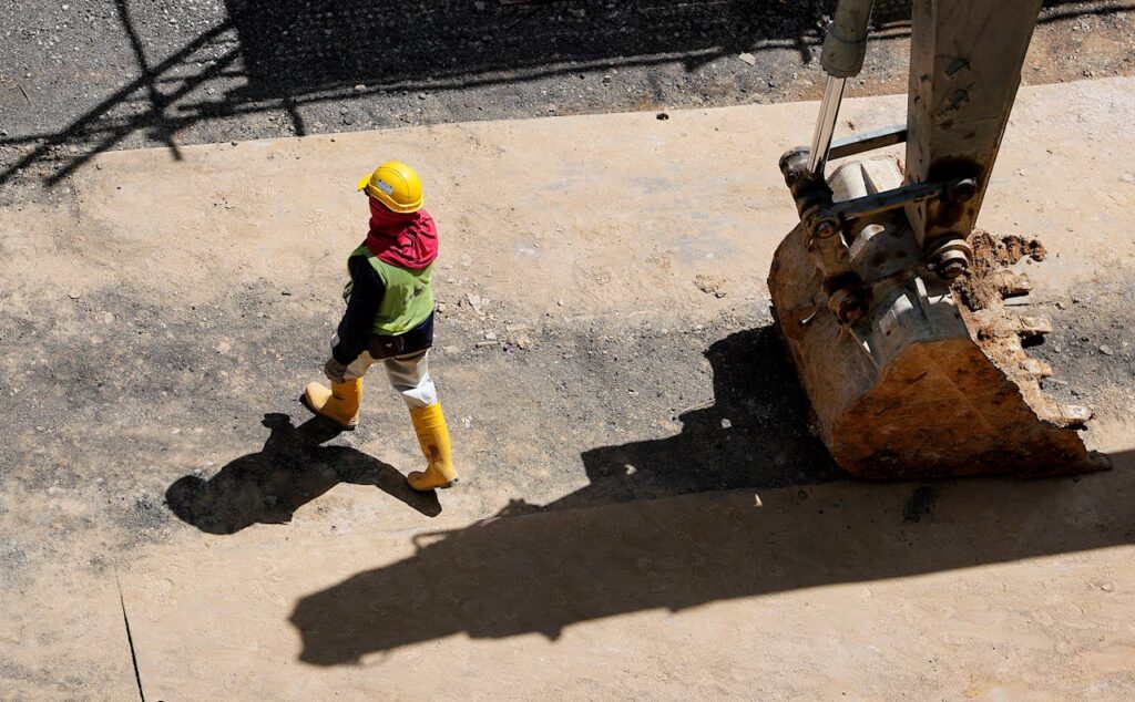 Overhead view of a construction worker walking beside a large excavator.