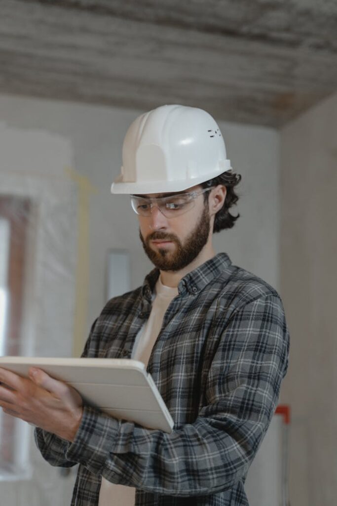 Male construction engineer assessing building plans indoors, wearing a hard hat.